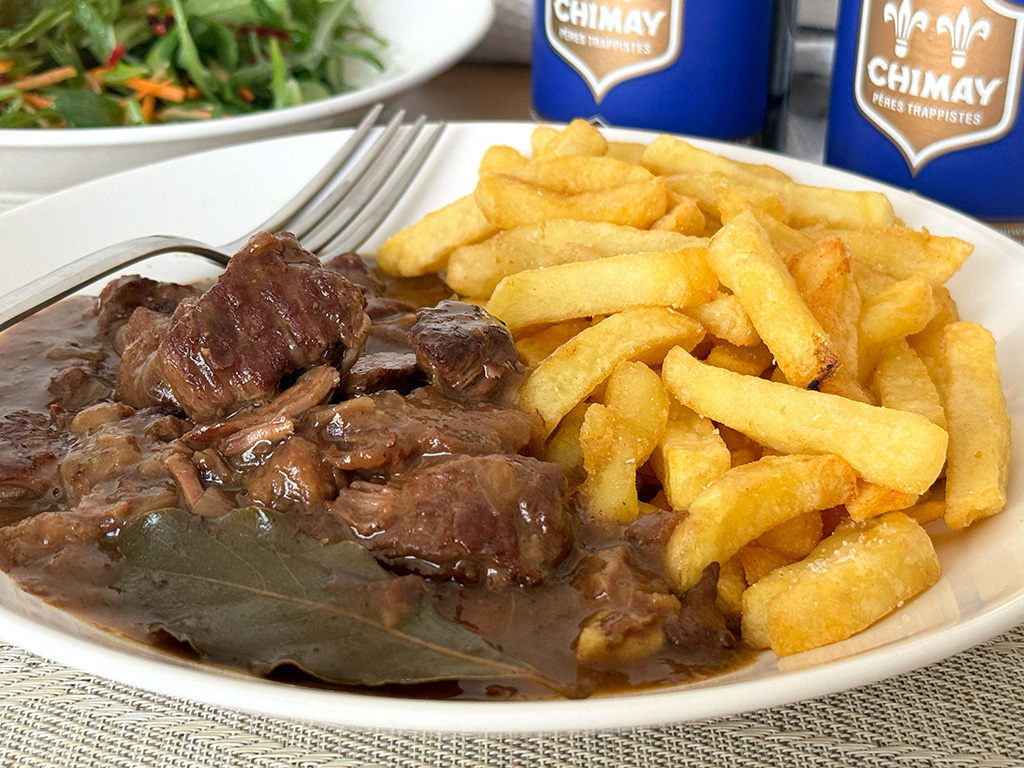 A plate of Flemish Beef Stew with fries, salad, and Belgian beer