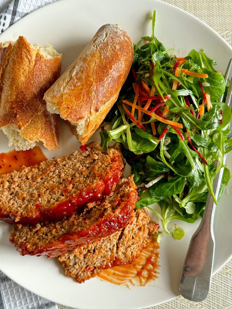 A plate of meatloaf from above, with a baguette and salad